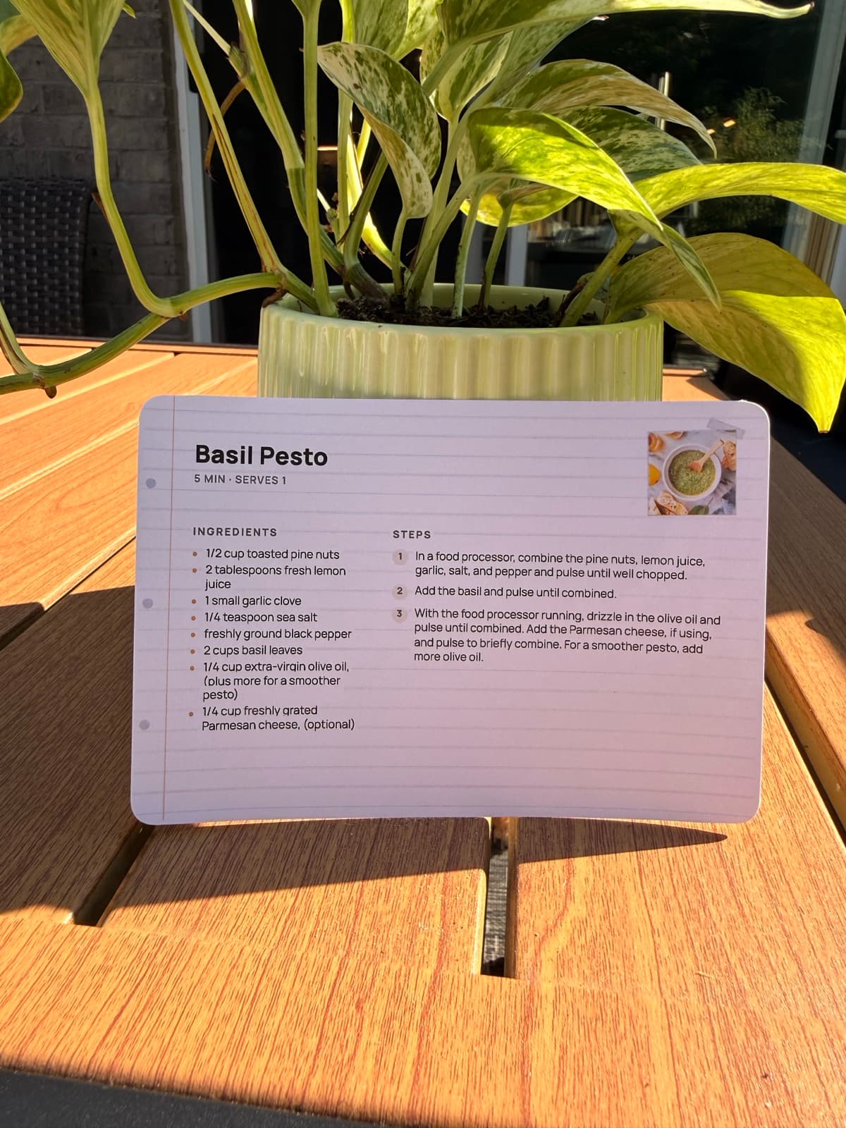 A basil pesto recipe card printed with RecipePrinter, standing on a sunny outdoor table.