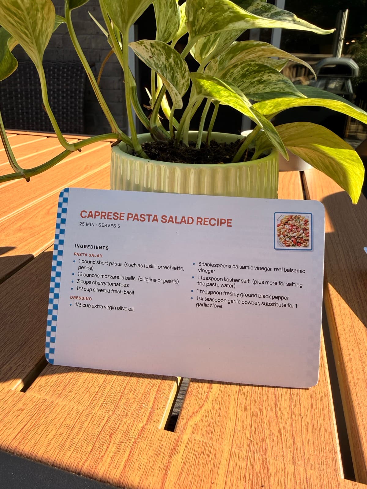 A Caprese pasta salad recipe card printed with RecipePrinter, standing on a sunny outdoor table.