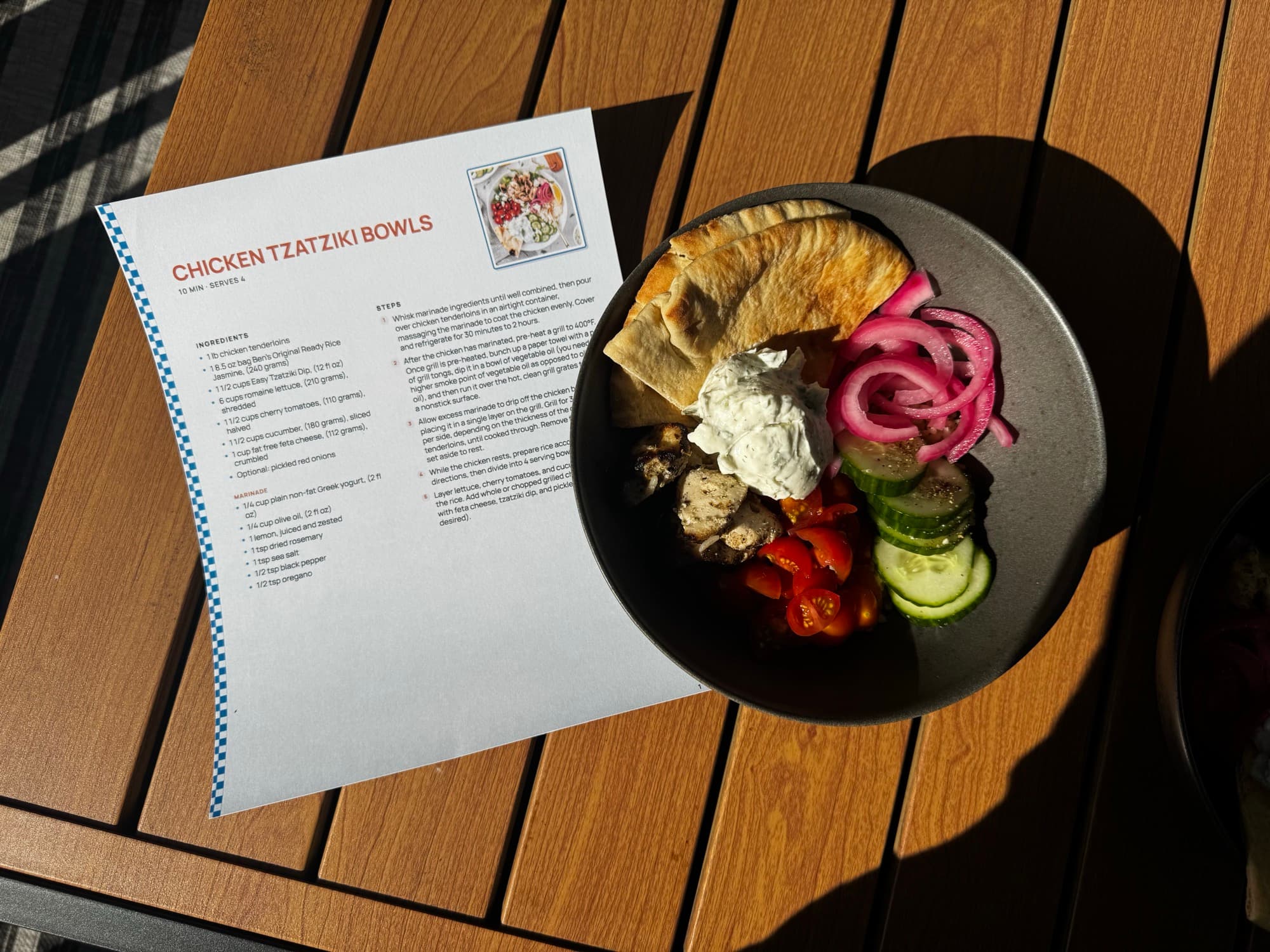 A printed full-page Chicken Tzatziki Bowls recipe on a garden table beside the finished bowl.