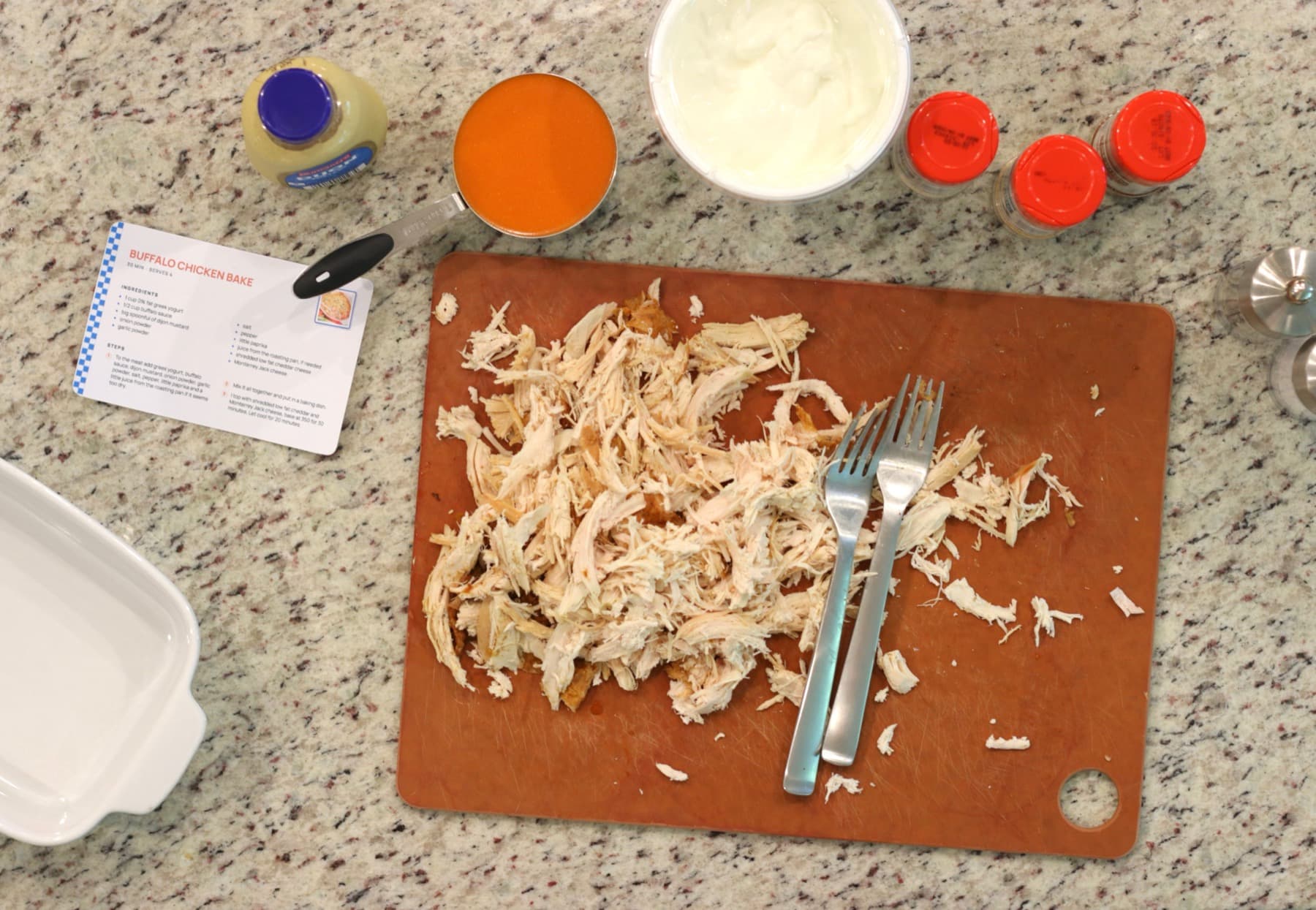A printed Buffalo Chicken Bake card on a kitchen counter beside the ingredients it calls for.