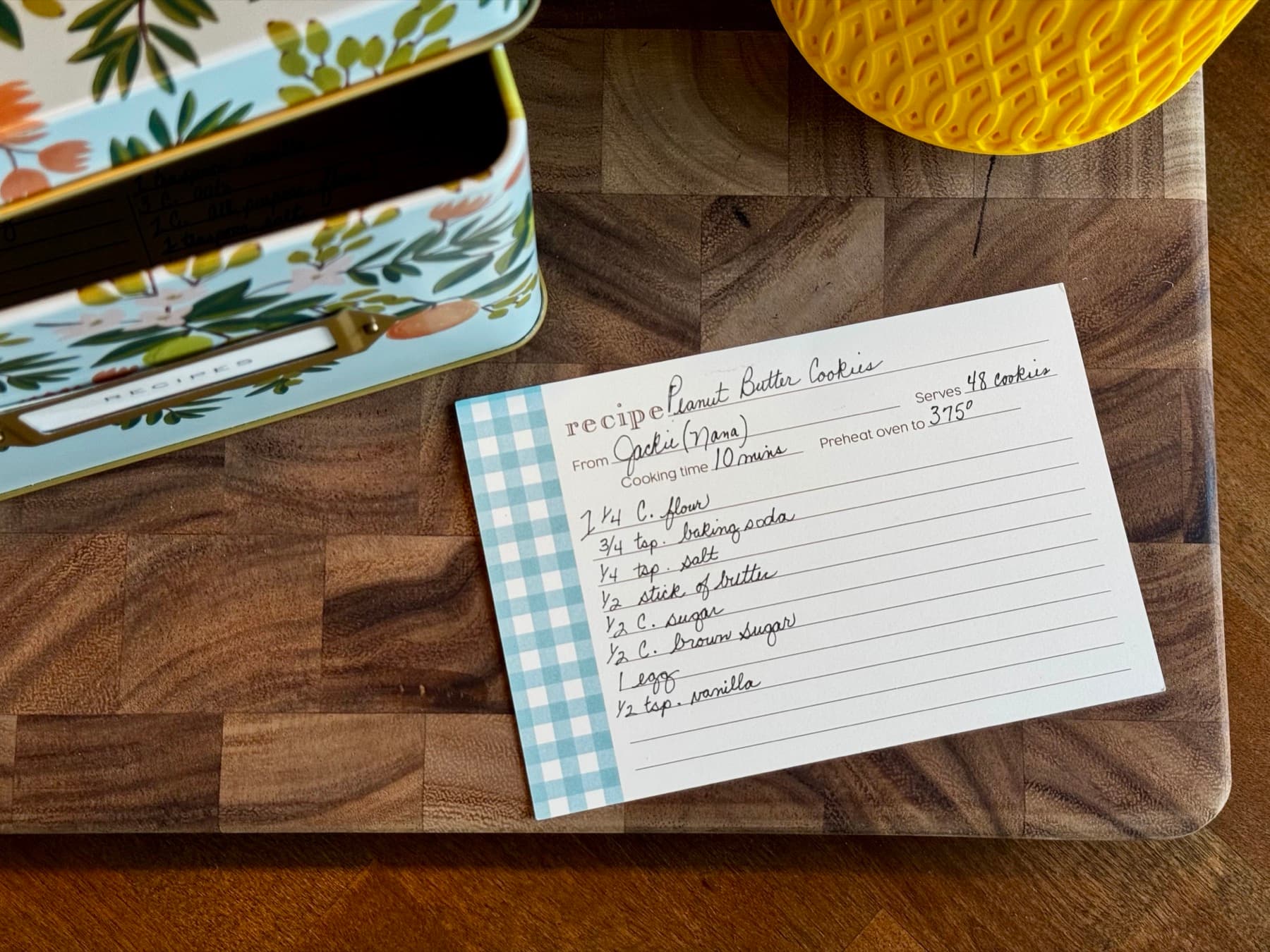 A handwritten Peanut Butter Cookies recipe card in cursive, lying beside an open floral recipe box.